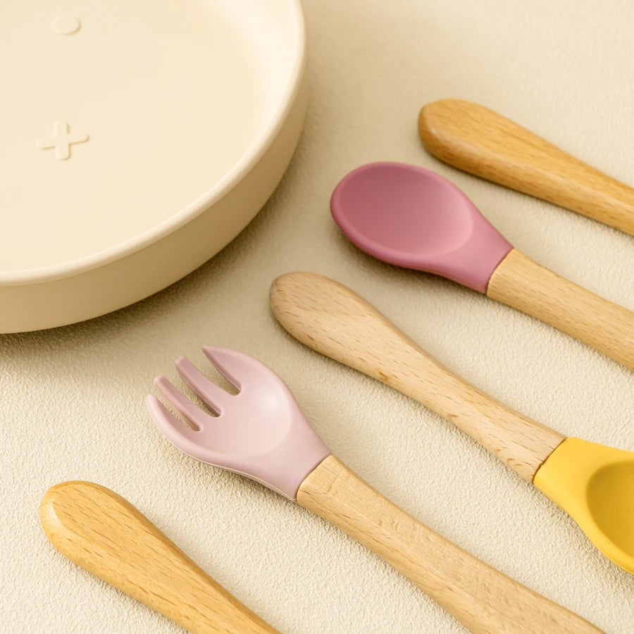 Présentation d’une fourchette et deux cuillères pour bébé en bois avec des embouts en silicone, coloré.