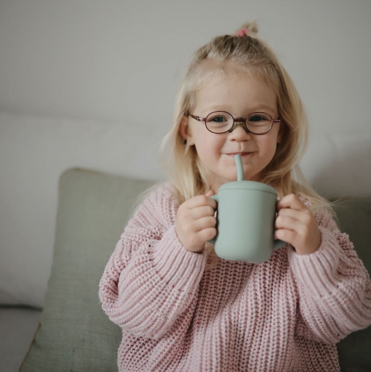 Présentation d’une enfant souriante qui bois avec une tasse verte.