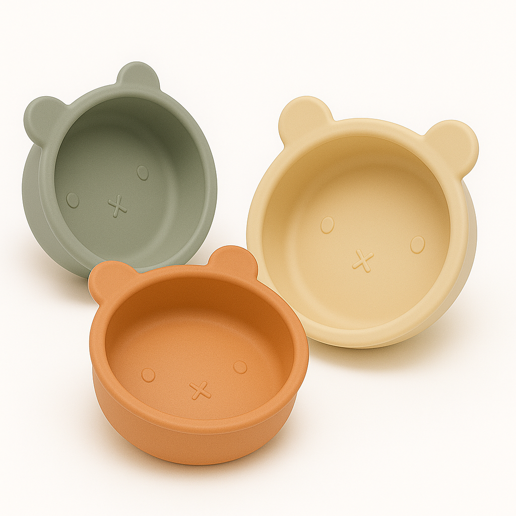 Présentation de trois bols pour enfants en silicone en forme d’ours, de couleur différente, un vert kaki, un beige et un orange sur un fond blanc
