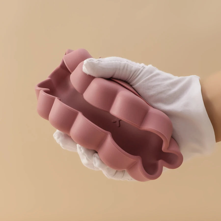 Présentation d'une assiette pour bébé en silicone rose, tenue par une main gantée.