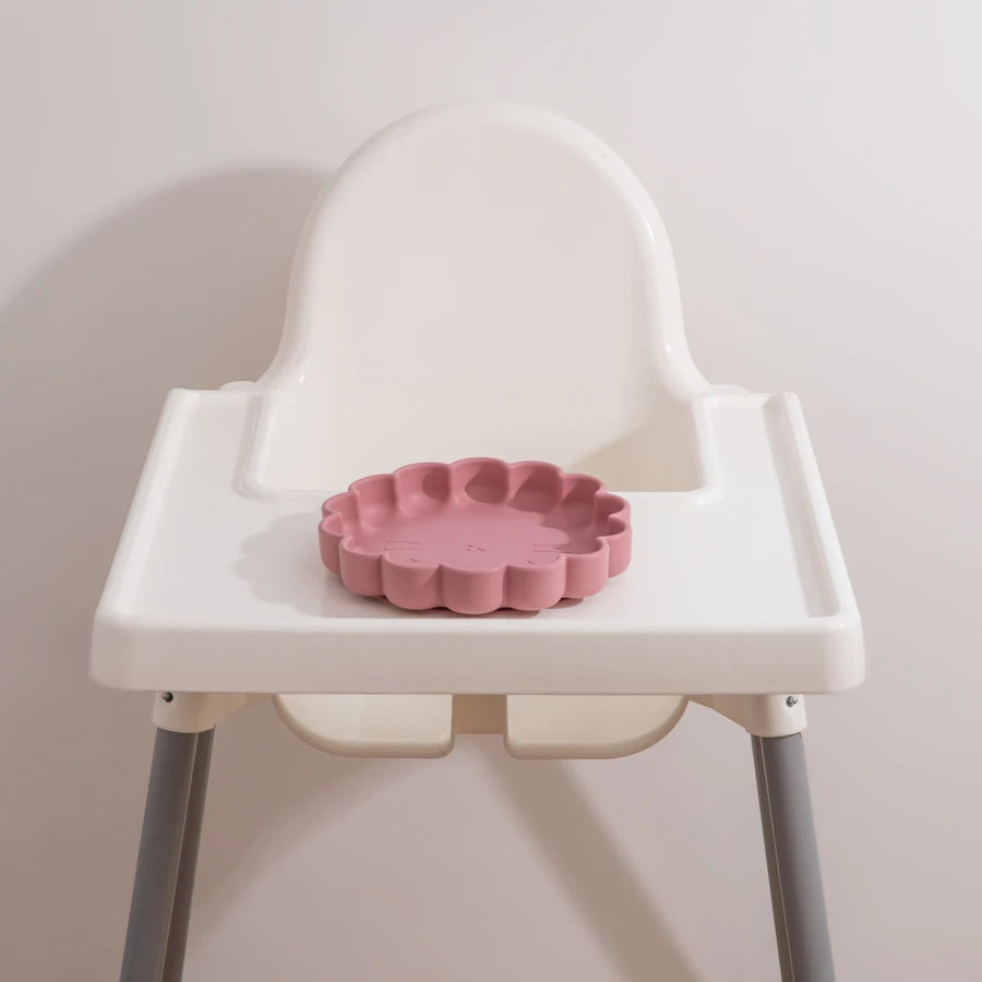 Présentation d'une assiette pour bébé en silicone rose sur le plateau d'une chaise haute blanche.