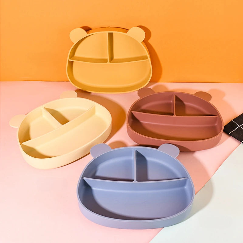 Présentation d'un ensemble d'assiettes pour bébé en silicone en forme d'ours, avec des compartiments et de différentes couleurs, disposées sur un fond uni.