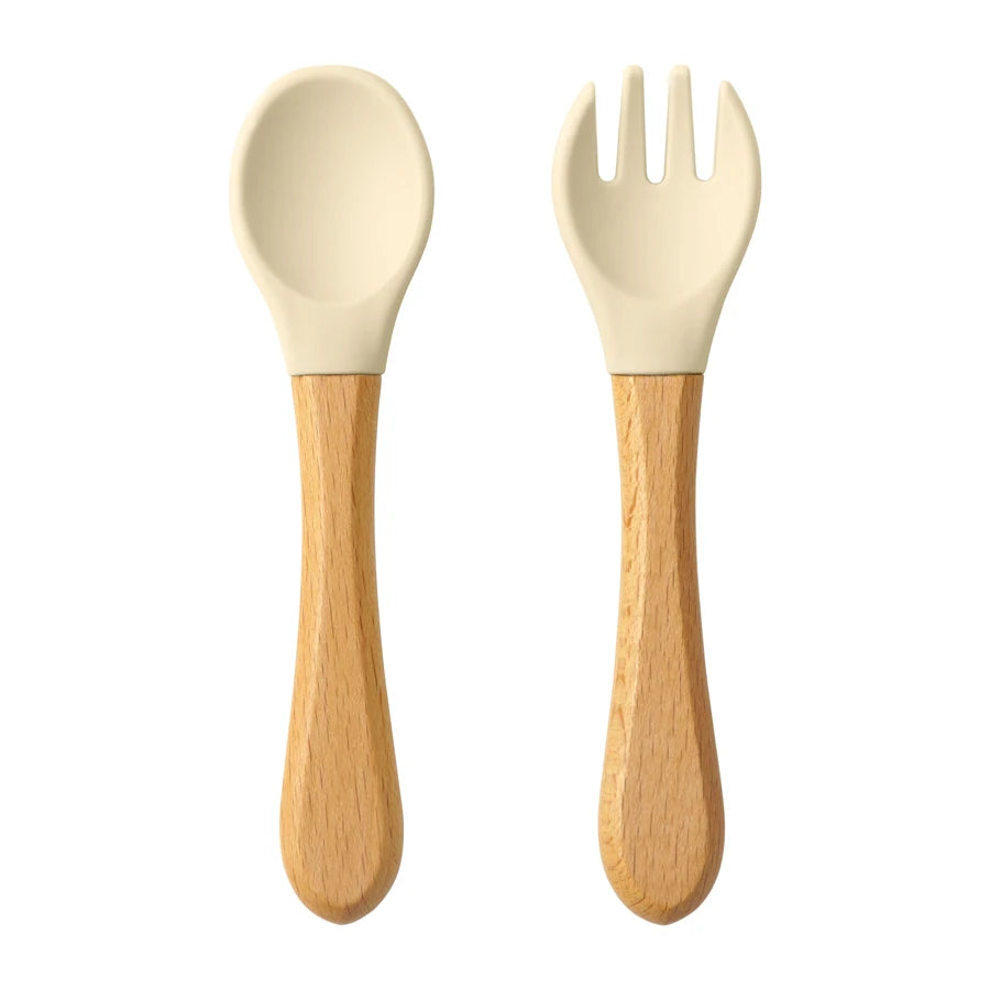 Présentation d’une fourchette et d’une cuillère pour bébé en bois avec des embouts silicone, beige.