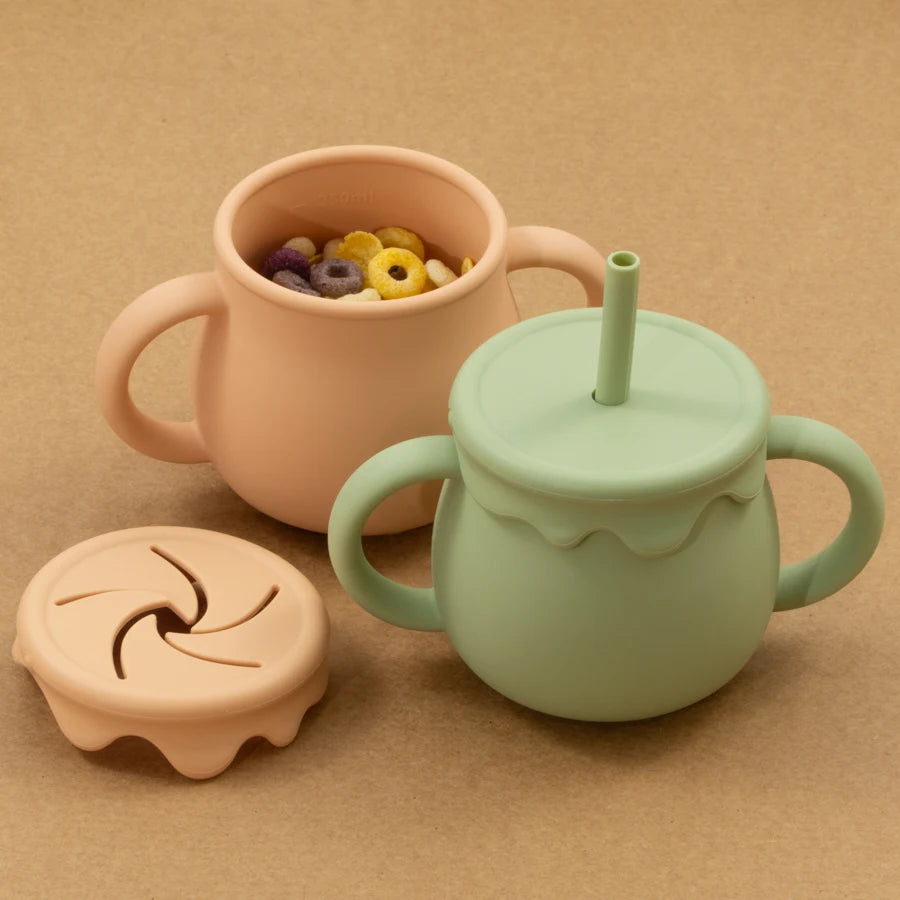 Présentation de deux tasses d'apprentissage pour bébé en silicone de différentes couleurs vert et orange, avec un couvercle amovible.