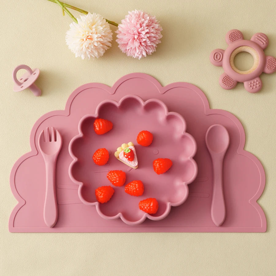Présentation d'un repas pour bébé servi dans une assiette en silicone rose, avec des couverts et des accessoires assortis.
