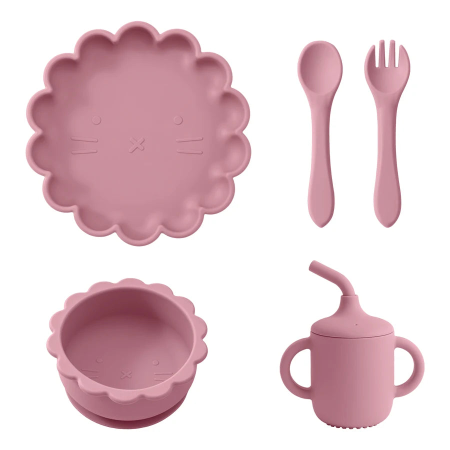 Présentation d'une assiette, d'un bol, d'un gobelet et de couverts pour bébé en silicone rose foncé.