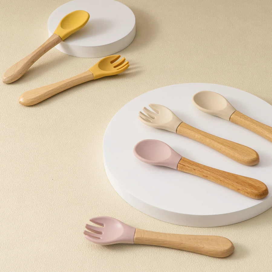 Présentation de fourchette et de cuillères pour bébé en bois, avec des embouts en silicone colorés.