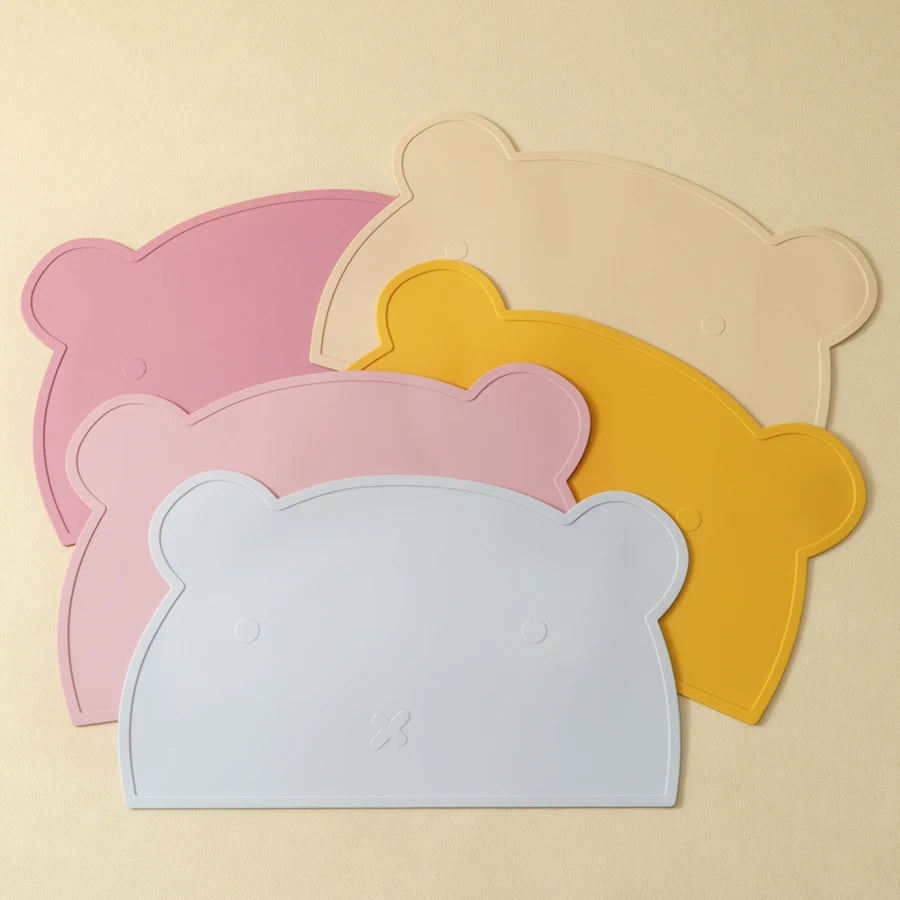 Présentation de sets de table pour bébé en silicone en forme d'ours empiler de différente couleurs (bleu clair, rose clair, jaune, beige et rose foncé).