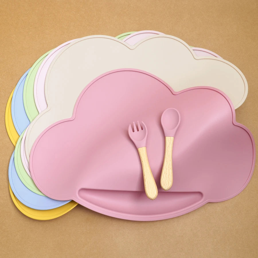 Présentation d'un ensemble de sets repas pour bébé en silicone de différentes couleurs, en forme de nuage, avec un set rose au premier plan et des couverts assortis.