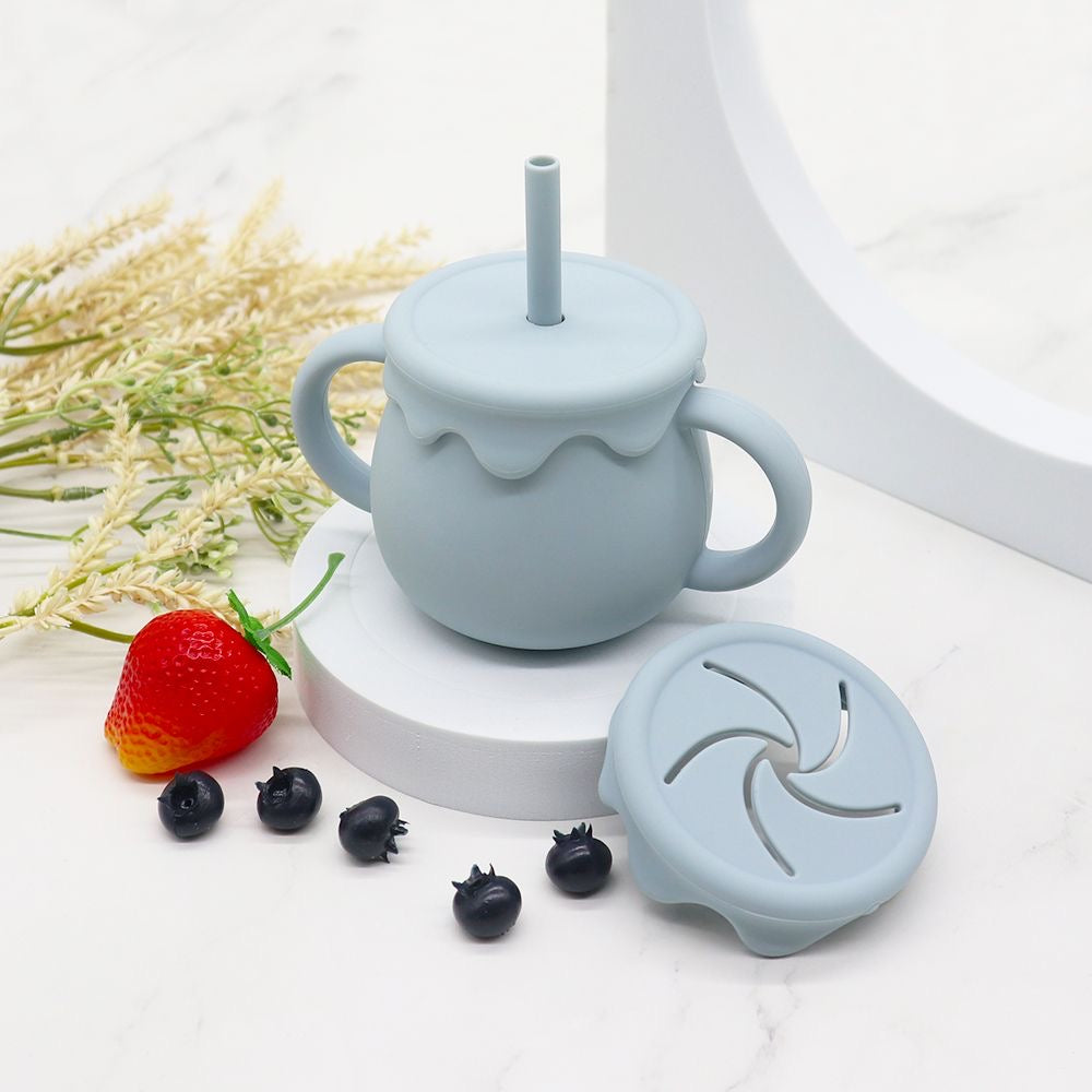 Présentation d'une tasse pour enfant bleu clair avec une paille et des anses, avec son couvercle et des fruits autour.