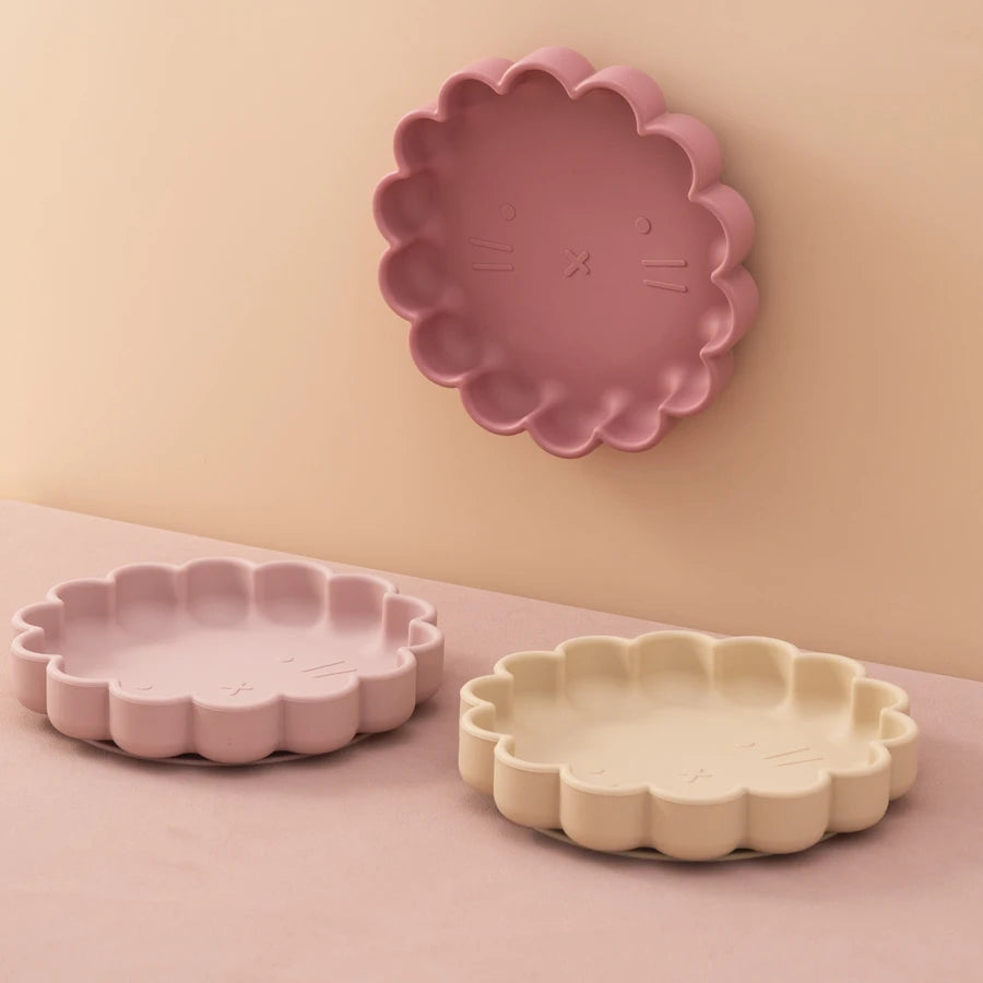 Présentation d'un trio d'assiettes pour bébé en silicone, de couleur rose clair, rose foncé, beige, avec deux assiettes en bas et une en haut.