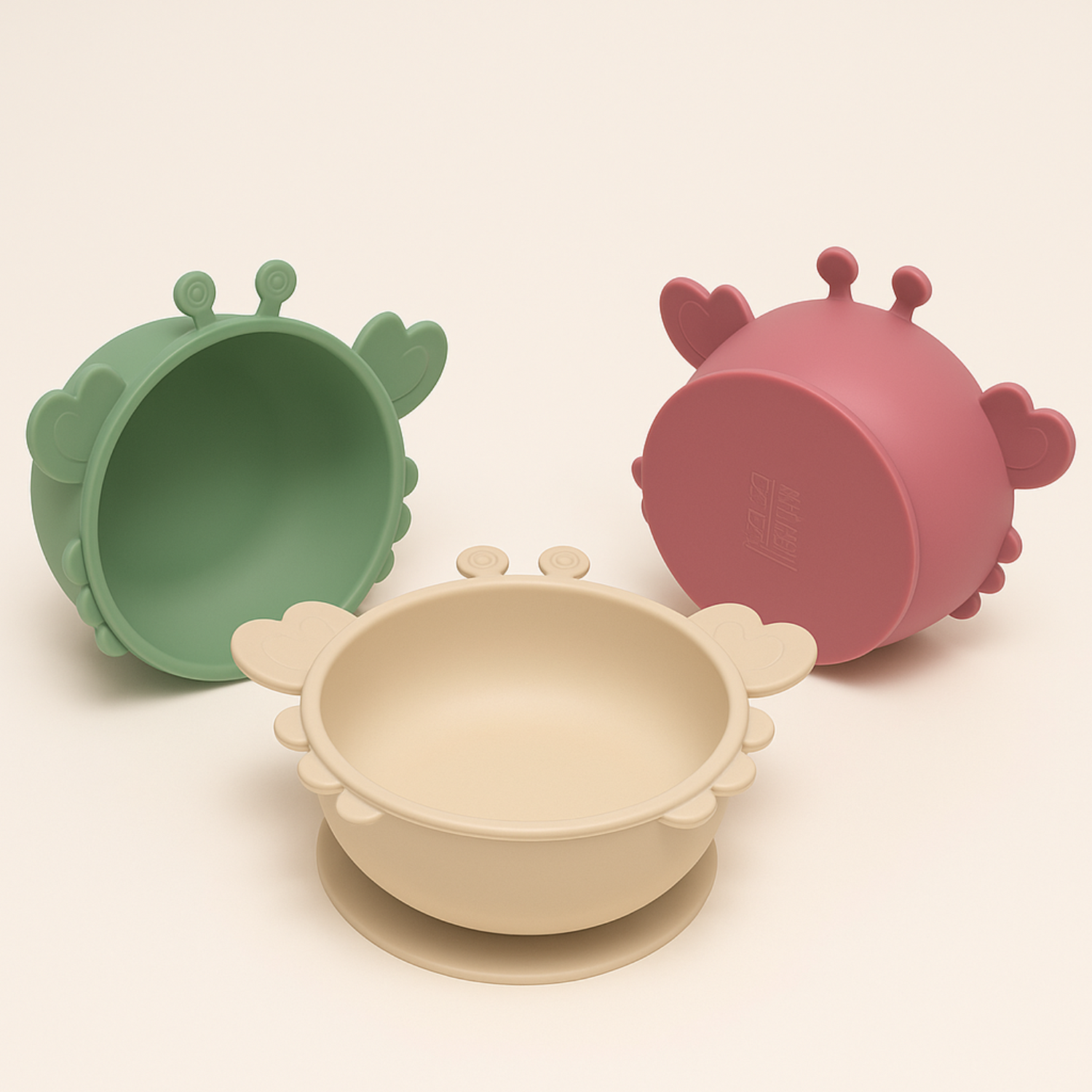 Présentation d’un trio de bol en silicone en forme de crabe de couleurs différentes : un beige, un rose, et un vert 