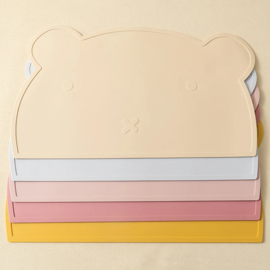 Présentation de sets de table pour bébé en silicone en forme d'ours empiler de différente couleurs (bleu clair, rose clair, jaune, beige et rose foncé).
