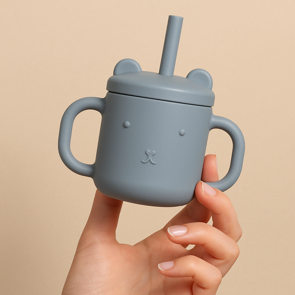 Présentation d’une Image produit où on voit une main de femme qui tient une tasse en silicone pour enfants de couleur bleu en forme de chat.
